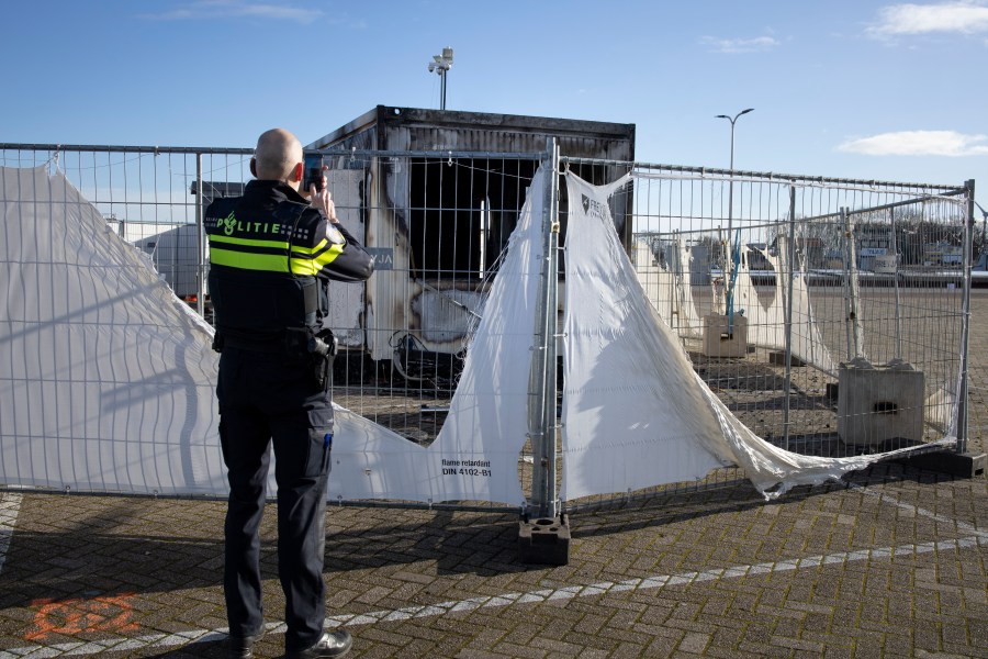 A police officer takes pictures of a burned-out coronavirus testing facility in the fishing village of Urk in the Netherlands on Jan. 24, 2021, after it was set on fire the night before by rioting youths protesting on the first night of a nationwide curfew. (Peter Dejong / Associated Press)