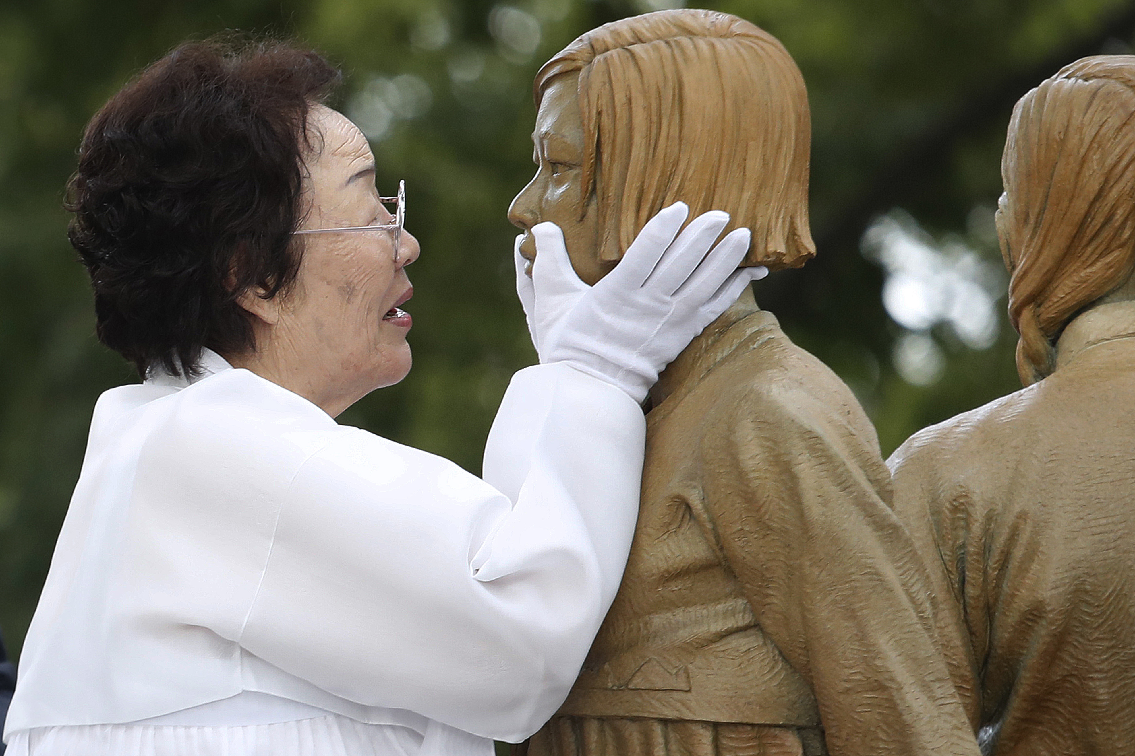 In this Aug. 14, 2019, file photo, Lee Yong-soo, who was forced to serve for the Japanese troops as a sex slave during World War II, touches the face of a statue of a girl symbolizing the issue of wartime "comfort women" during its unveiling ceremony in Seoul, South Korea. (AP Photo/Ahn Young-joon, File)