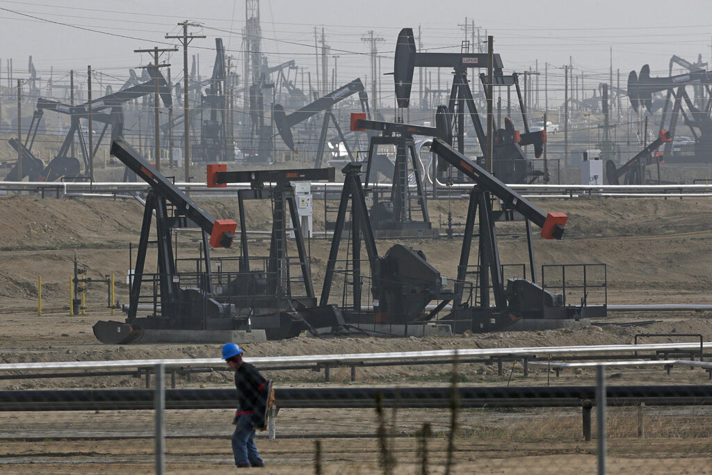 In this Jan. 16, 2015, file photo, a person walks past pump jacks operating at the Kern River Oil Field in Bakersfield, Calif. (AP Photo/Jae C. Hong, File)