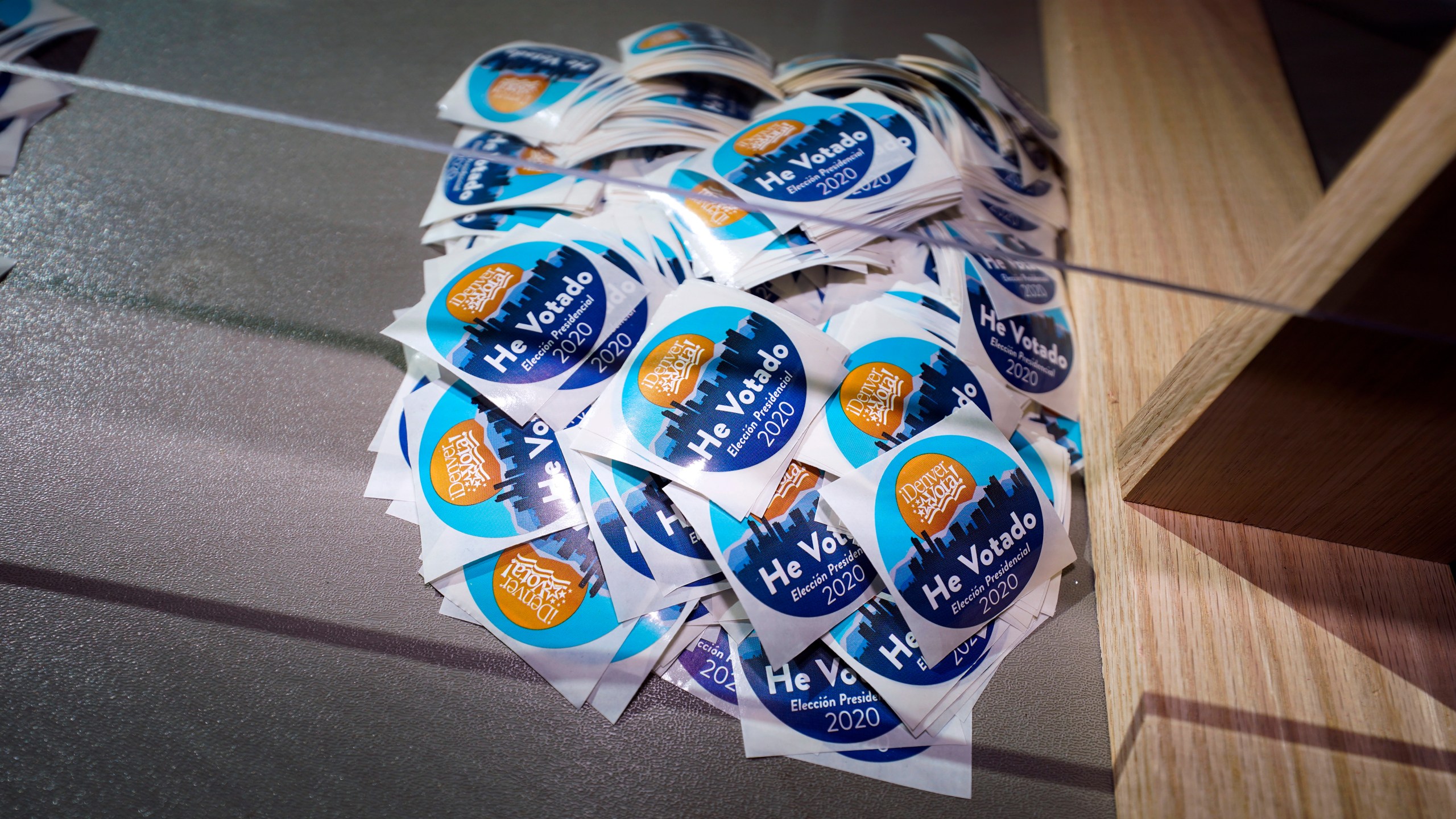 In this Oct. 30, 2020, file photo stickers printed in Spanish sit on the desk of an election judge to be distributed to voters after they cast their ballots in the atrium of Ball Arena, the home of the NBA's Denver Nuggets and the NHL's Colorado Avalanche in Denver. (AP Photo/David Zalubowski, File)