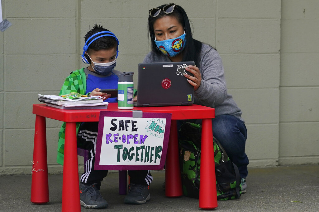 In this Thursday, Feb. 18, 2021, file photo, Maya Peralta, right, sits with her son, Clarendon Alternative Elementary School second-grader H Suchovsky, as students and parents attend distance learning Zoom classes at Midtown Terrace Playground in San Francisco. (AP Photo/Jeff Chiu, File)