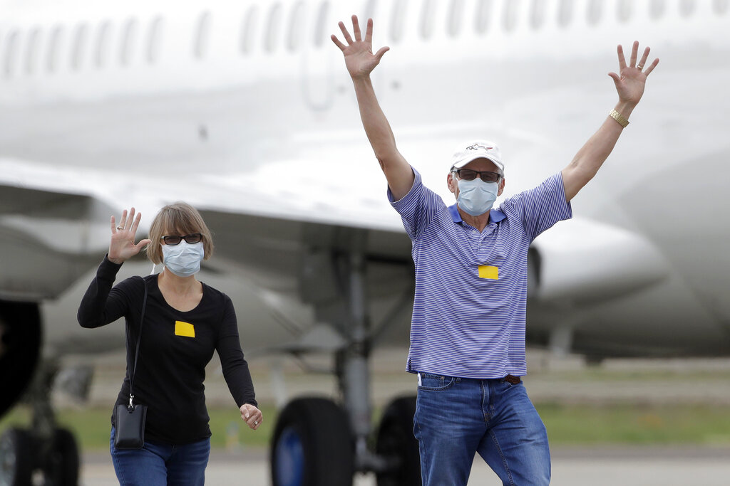 In this March 10, 2020, file photo, passengers from the Grand Princess, a cruise ship carrying multiple people who have tested positive for COVID-19, gesture toward reporters while walking on a tarmac before boarding a chartered plane in Oakland, Calif., on March 10, 2020. (AP Photo/Jeff Chiu, File)