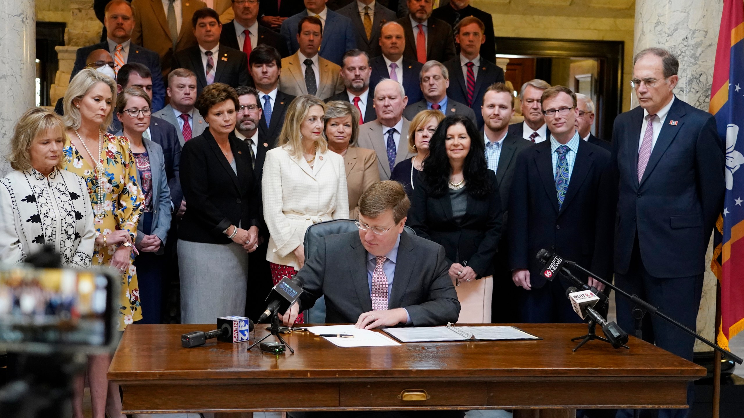 Mississippi Gov. Tate Reeves signs the first state bill in the U.S. this year to ban transgender athletes from competing on female sports teams, as supporting lawmakers gather behind him, Thursday, March 11, 2021, at the Capitol in Jackson, Miss. (AP Photo/Rogelio V. Solis)