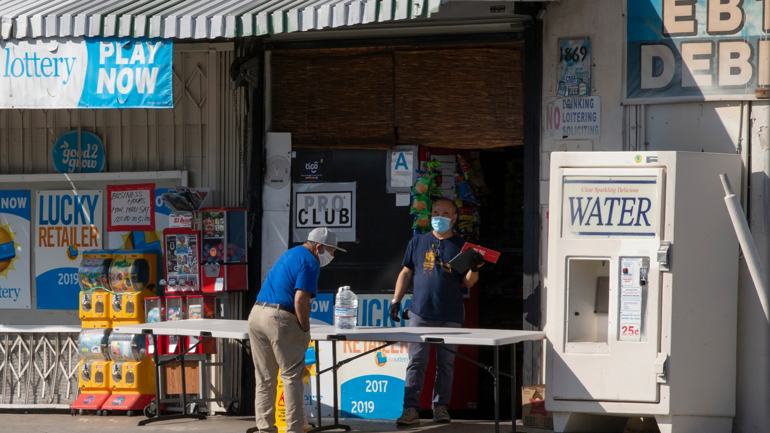 In this April 1, 2020, file photo, a customer wears a face mask as he purchases drinking water at a "Grab-and-Go" market table in the Boyle Heights area of Los Angeles. (AP Photo/Damian Dovarganes, File)