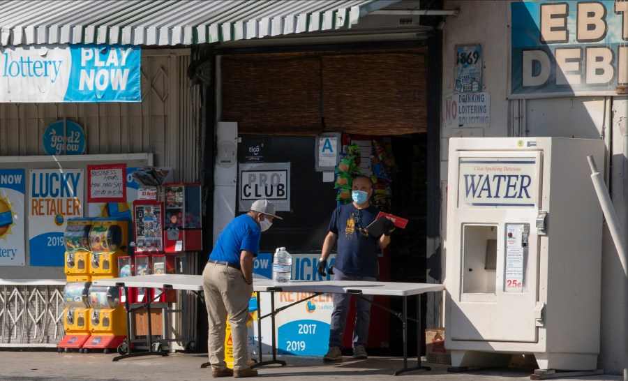 In this April 1, 2020, file photo, a customer wears a face mask as he purchases drinking water at a "Grab-and-Go" market table in the Boyle Heights area of Los Angeles. (AP Photo/Damian Dovarganes, File)