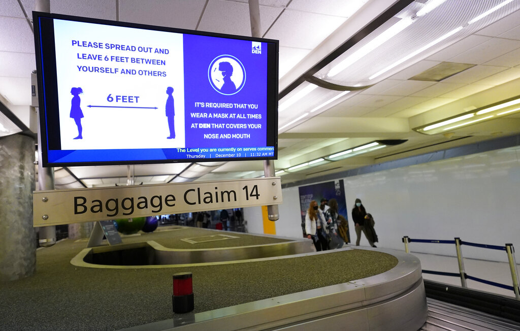 In this Dec. 10, 2020, file photo, an electronic sign warns travelers to maintain social distance in the terminal of Denver International Airport in Denver. (AP Photo/David Zalubowski, File)