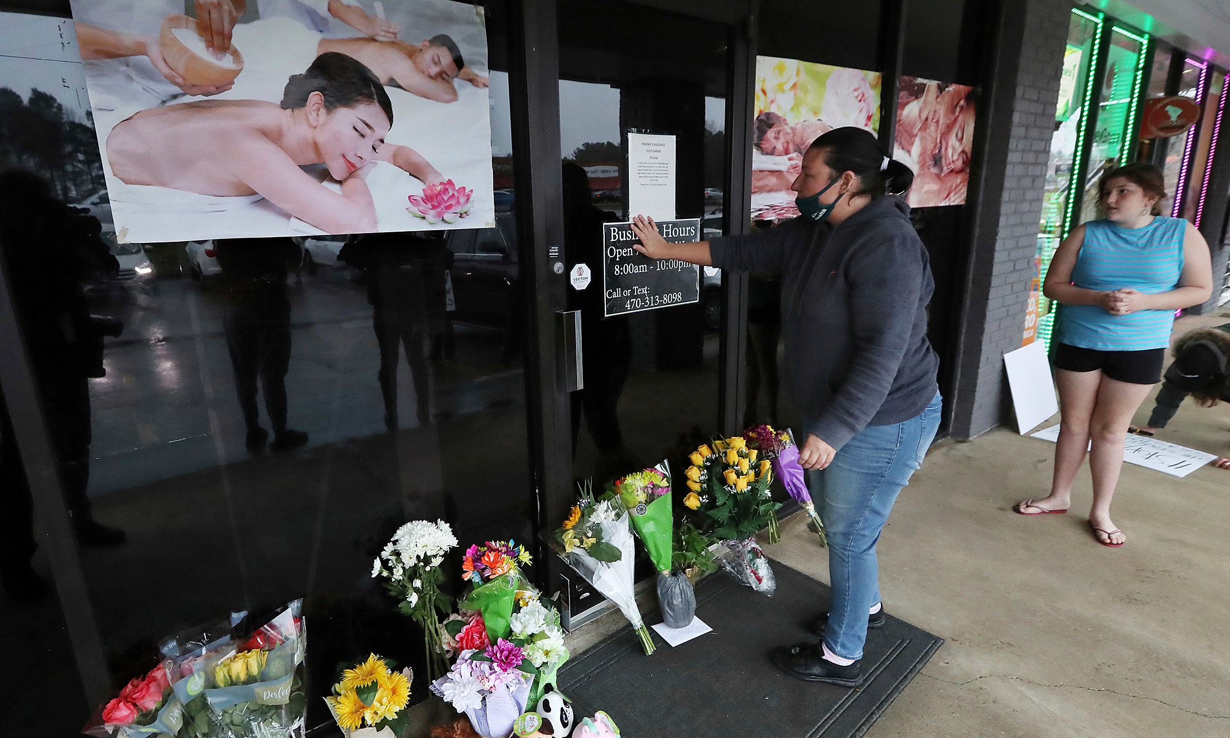 In this March 17, 2021, file photo, Jessica Lang pauses and places her hand on the door in a moment of grief after dropping off flowers with her daughter Summer at Youngs Asian Massage parlor where four people were killed in Acworth, Ga. (Curtis Compton/Atlanta Journal-Constitution via AP, File)