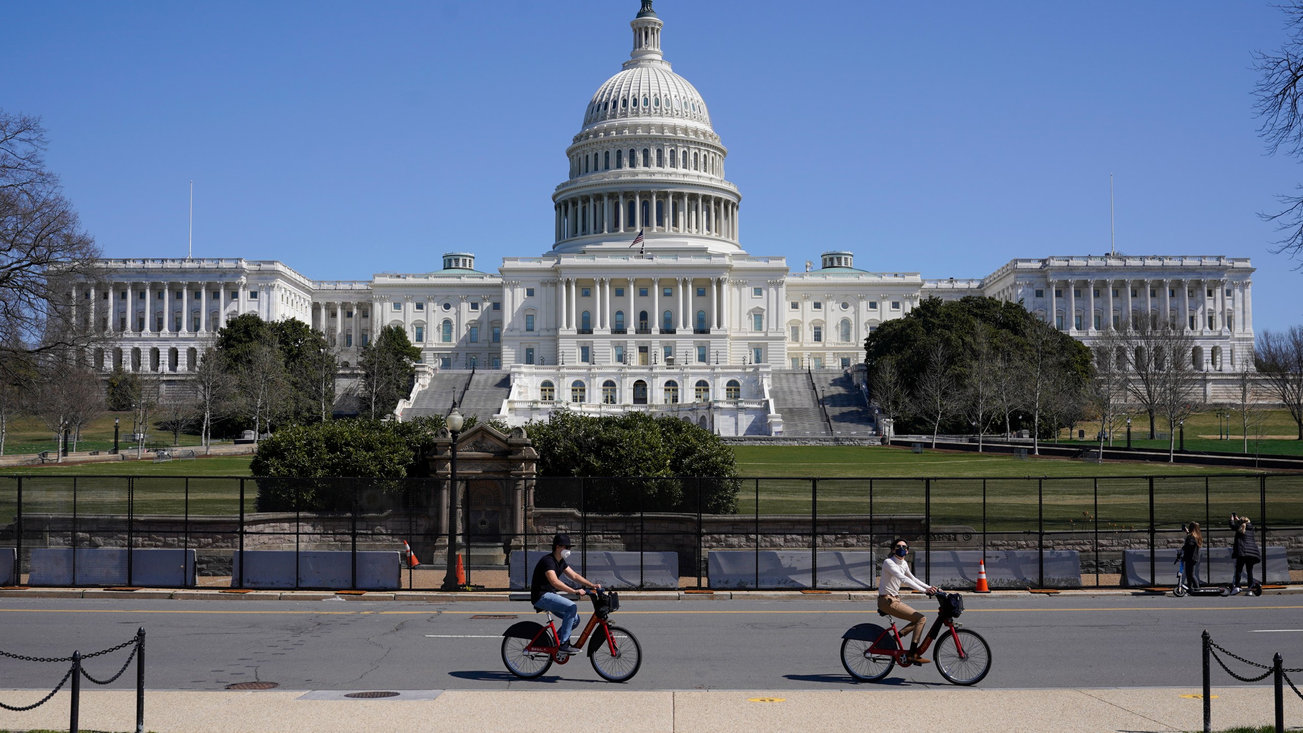 Bicyclists ride past an inner perimeter of security fencing on Capitol Hill in Washington, Sunday, March 21, 2021, after portions of an outer perimeter of fencing were removed overnight to allow public access. (AP Photo/Patrick Semansky)