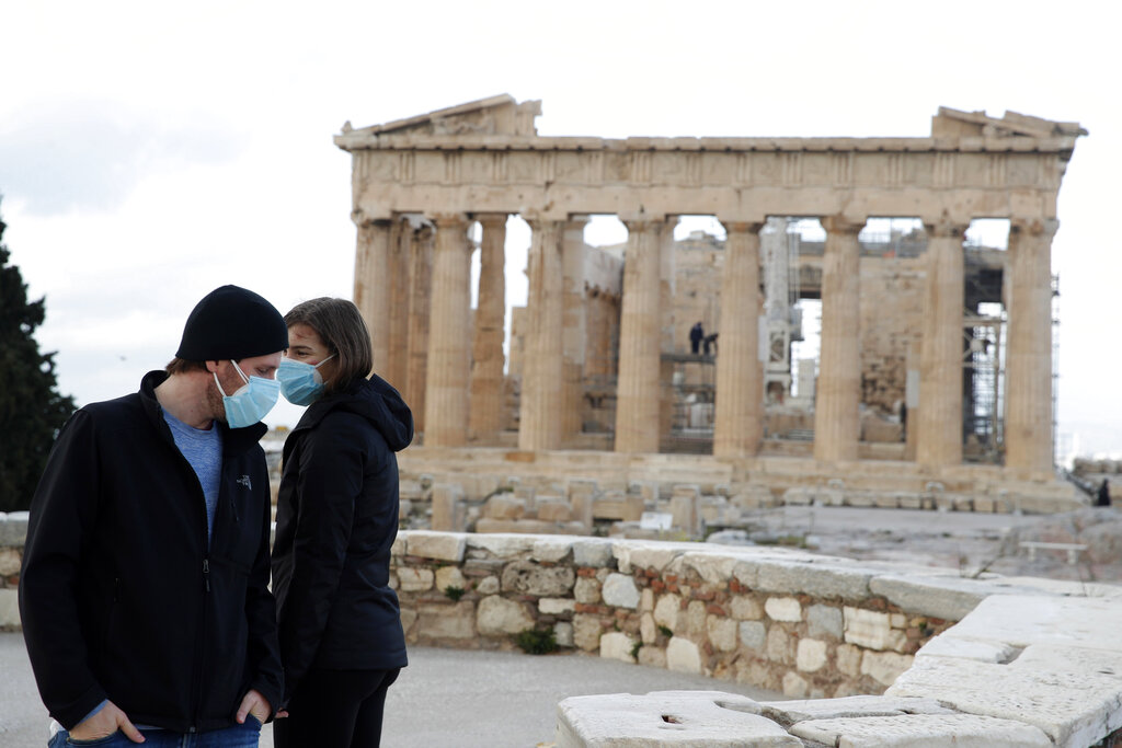 The first visitors wearing face masks to protect against the spread of coronavirus, stand atop of Acropolis hill, with the Parthenon temple in the background, in Athens, Monday, March 22, 2021. (AP Photo/Thanassis Stavrakis)