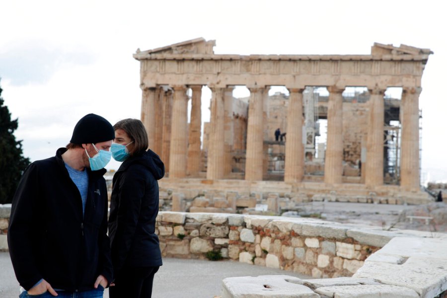 The first visitors wearing face masks to protect against the spread of coronavirus, stand atop of Acropolis hill, with the Parthenon temple in the background, in Athens, Monday, March 22, 2021. (AP Photo/Thanassis Stavrakis)