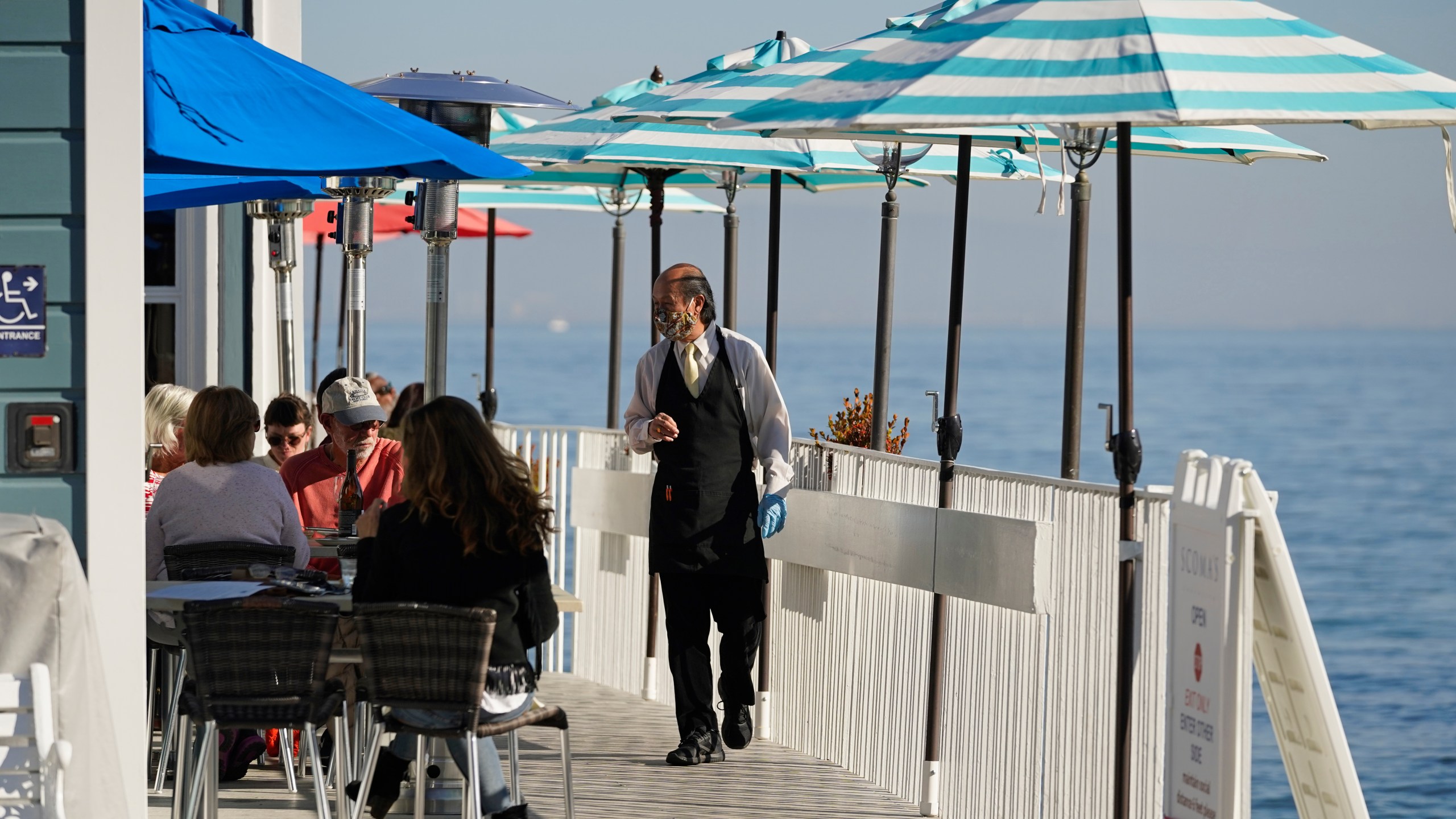 A waiter walks past tables of people dining outdoors in Marin County at Scoma's restaurant in Sausalito on Dec. 4, 2020. (Eric Risberg / Associated Press)