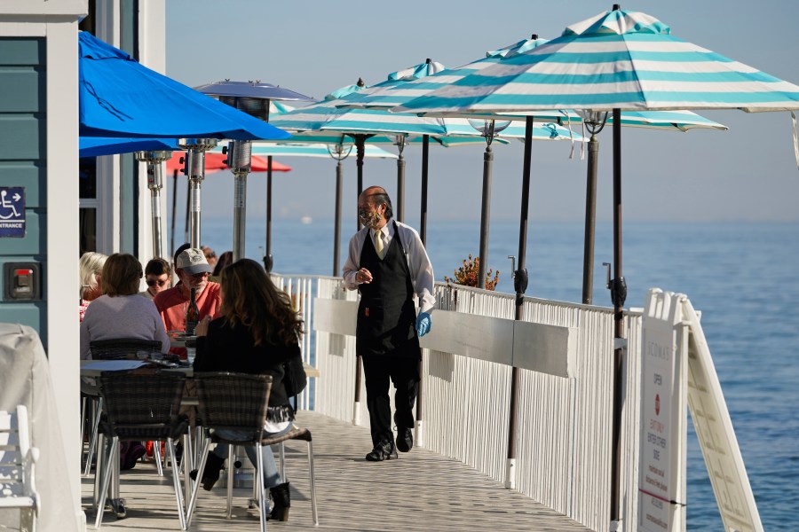 A waiter walks past tables of people dining outdoors in Marin County at Scoma's restaurant in Sausalito on Dec. 4, 2020. (Eric Risberg / Associated Press)