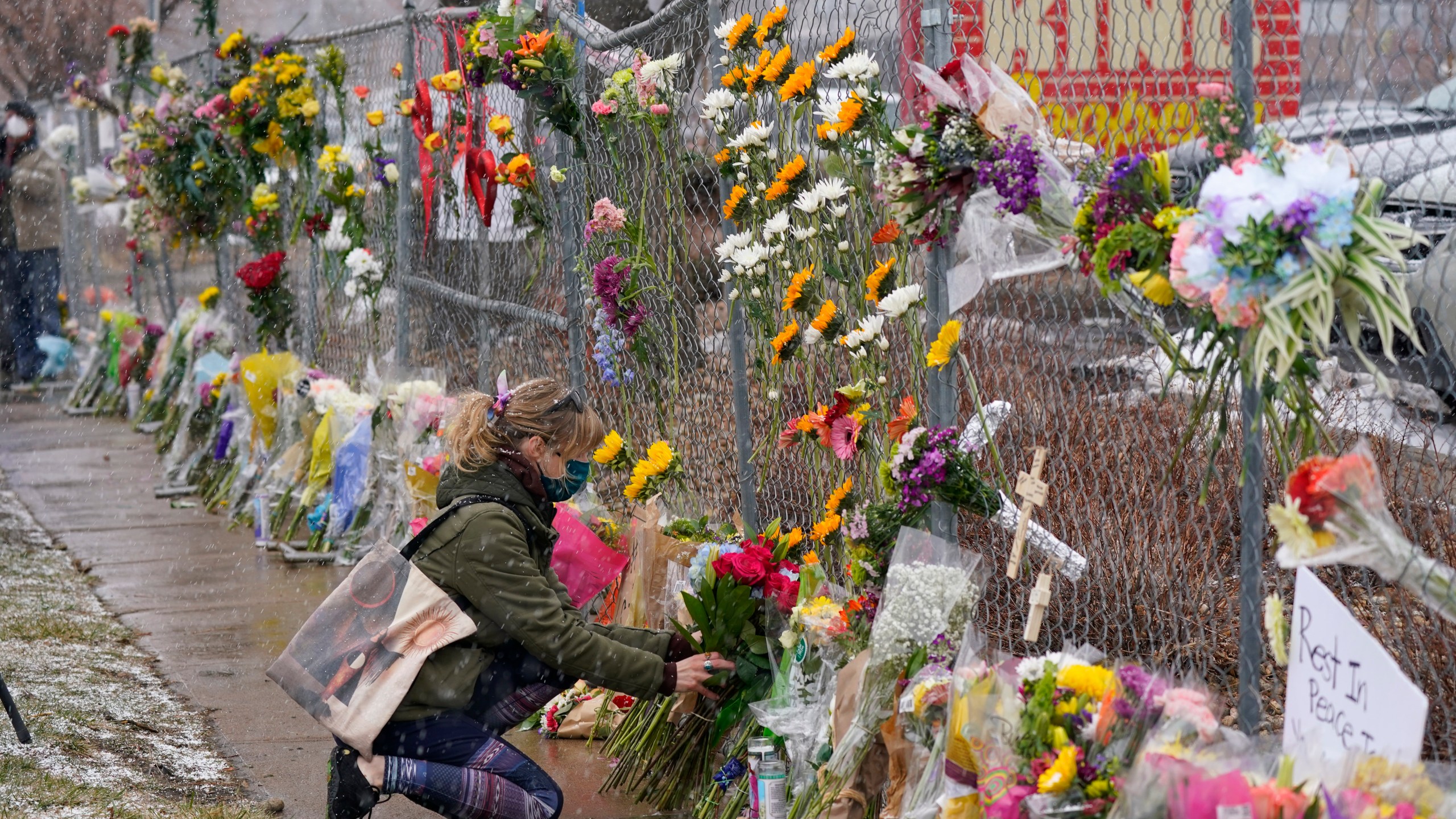 A mourner leaves a bouquet of flowers along a fence put up around the parking lot where a mass shooting took place in a King Soopers grocery store Tuesday, March 23, 2021, in Boulder, Colo. (AP Photo/David Zalubowski)