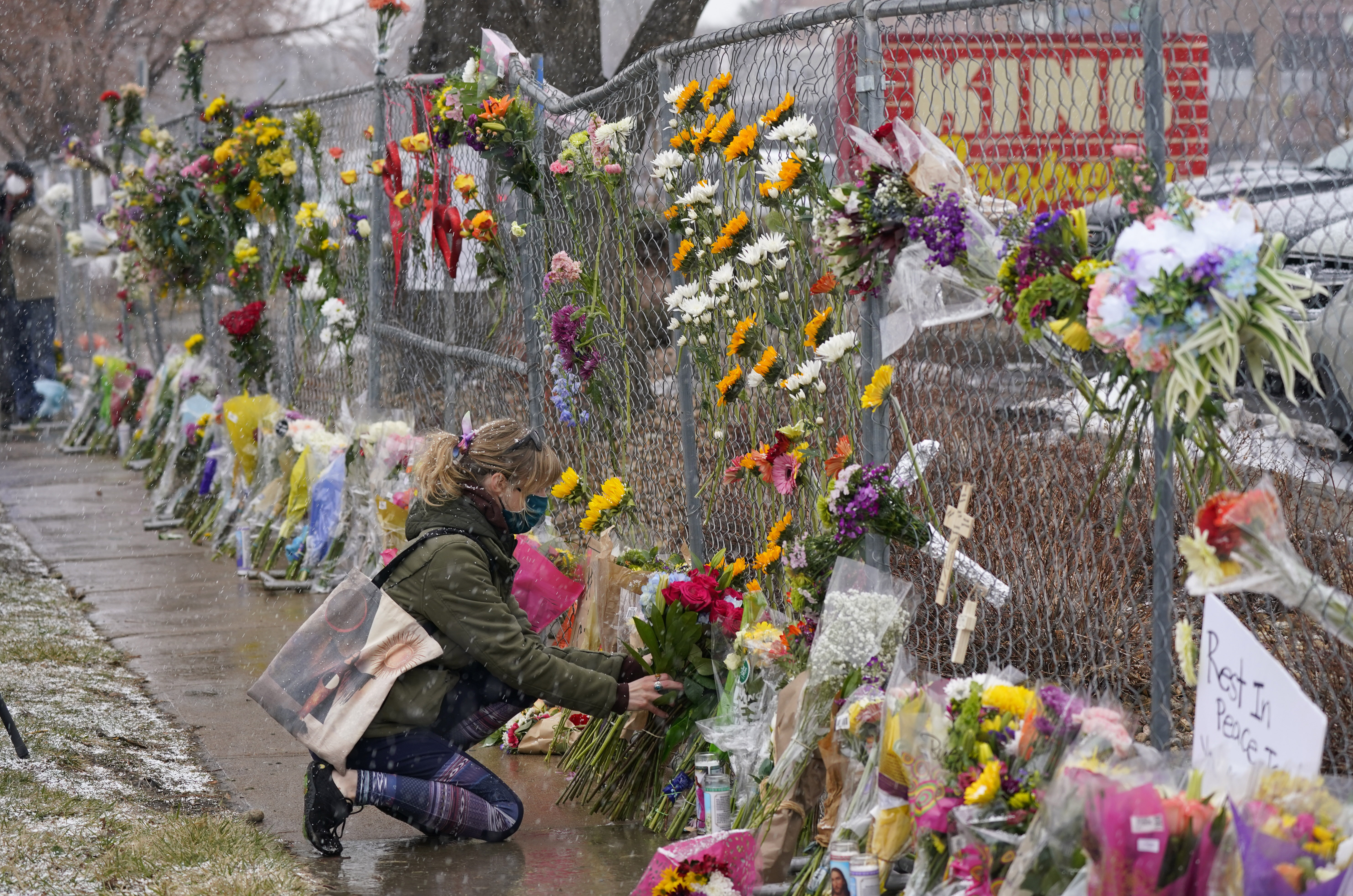 A mourner leaves a bouquet of flowers along a fence put up around the parking lot where a mass shooting took place in a King Soopers grocery store Tuesday, March 23, 2021, in Boulder, Colo. (AP Photo/David Zalubowski)