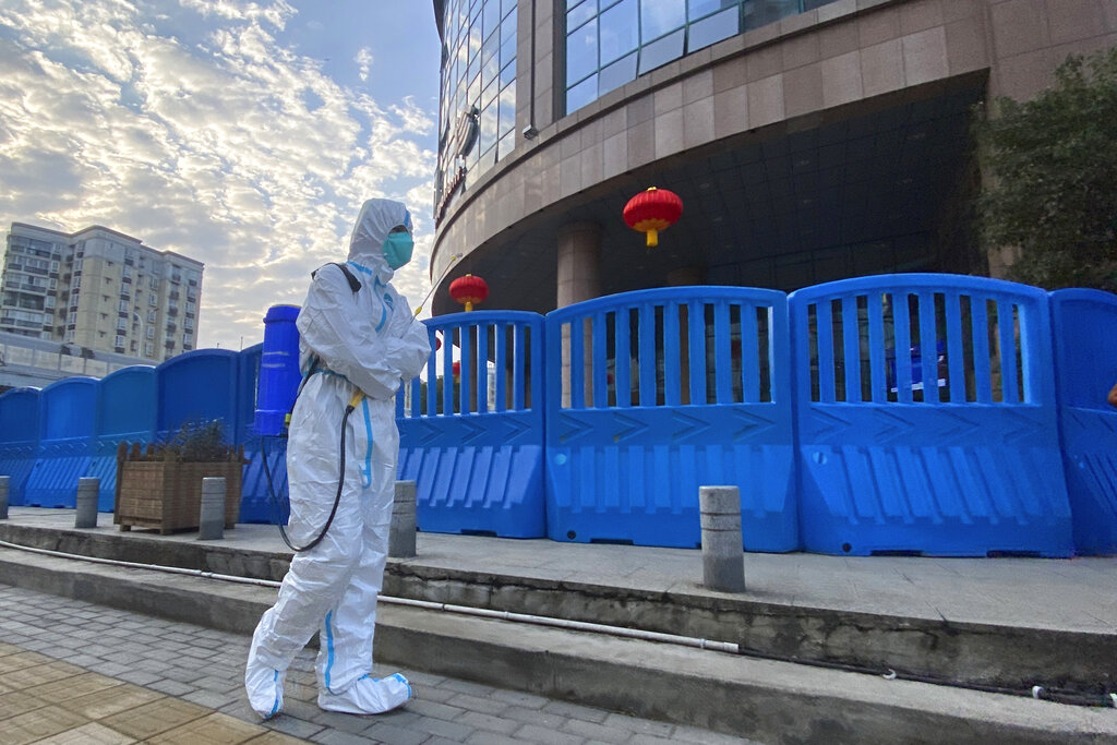 In this file photo dated Saturday, Feb. 6, 2021, a worker in protectively overalls and carrying disinfecting equipment walks outside the Wuhan Central Hospital where Li Wenliang, the whistleblower doctor who sounded the alarm and was reprimanded by local police for it in the early days of Wuhan's pandemic, worked in Wuhan in central China. A lengthy written report published Thursday March 25, 2021, from a team of international and Chinese scientists on a joint mission to Wuhan aims to help unearth the origins of the coronavirus since it was first detected in China more than a year ago. (AP Photo/Ng Han Guan, FILE)