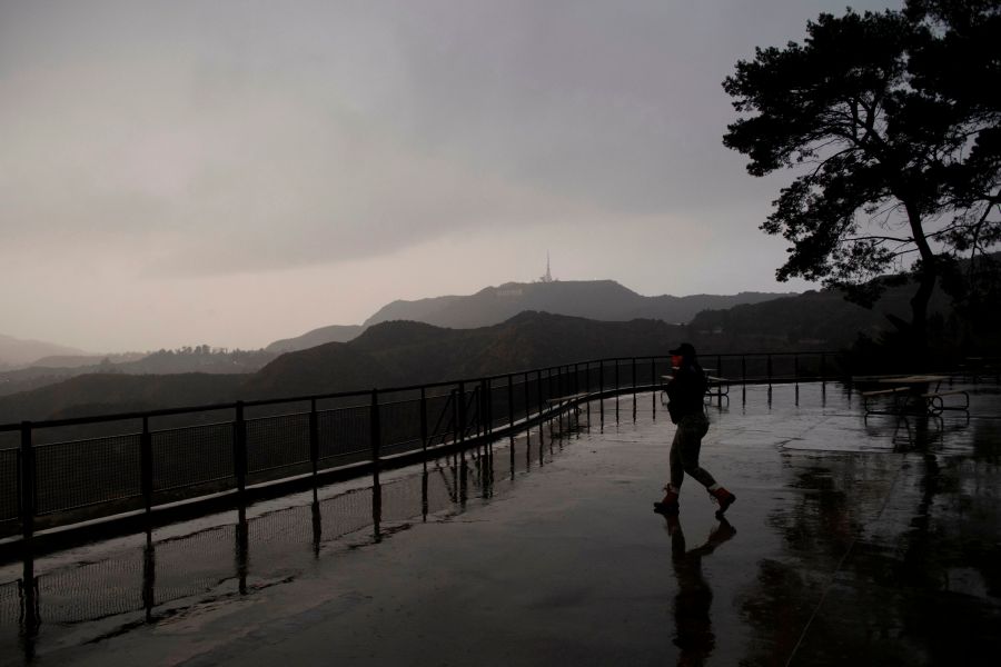 A person wears a face mask while walking to take pictures from a viewing area overlooking the Hollywood sign shrouded by clouds during heavy rains as seen from the Griffith Observatory on Dec. 28, 2020, in Los Angeles, California. (Patrick T. Fallon/AFP via Getty Images)