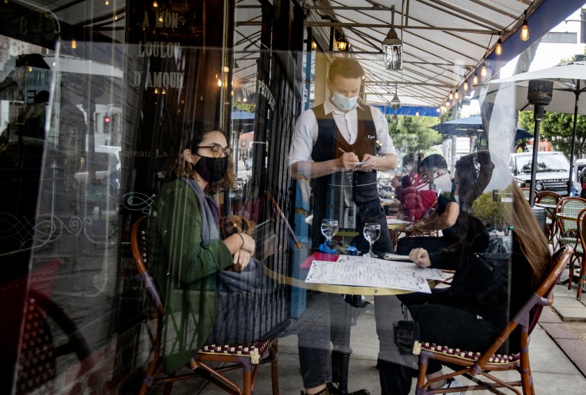 A waiter serves customers behind a plexiglass partition at Figaro Bistrot in Los Feliz on the first day that Los Angeles County again allowed indoor seating at restaurants in March 2021. (Gina Ferazzi/ Los Angeles Times)