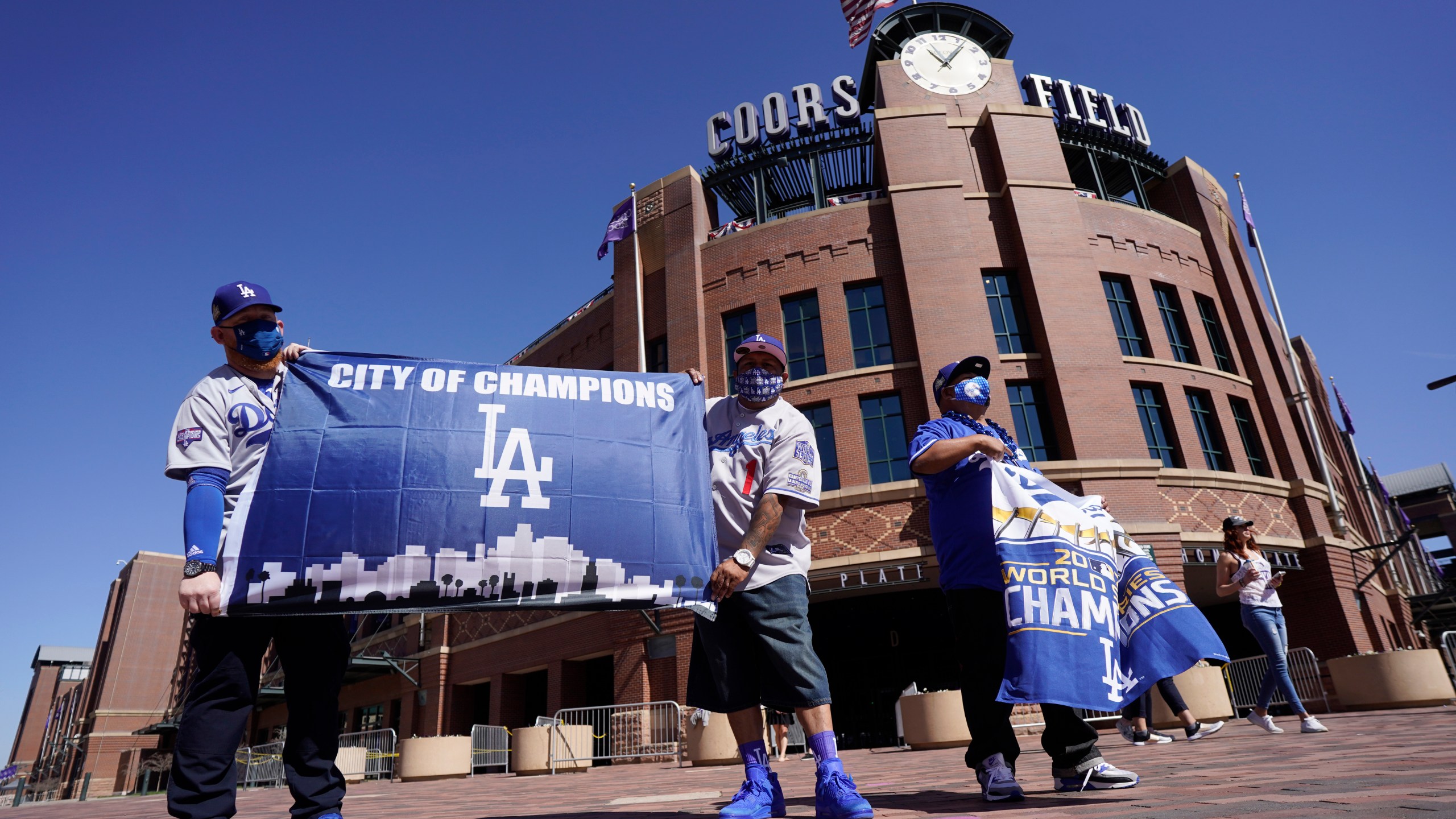 Los Angeles Dodgers fans Oliver Olson, left, of San Diego, Juan Campo and Rudy Soto, both of Los Angeles, hold up flags outside the main entrance to Coors Field in Denver as fans return for the first inning of a baseball game between the Dodgers and Colorado Rockies on April 1, 2021. (David Zalubowski / Associated Press)