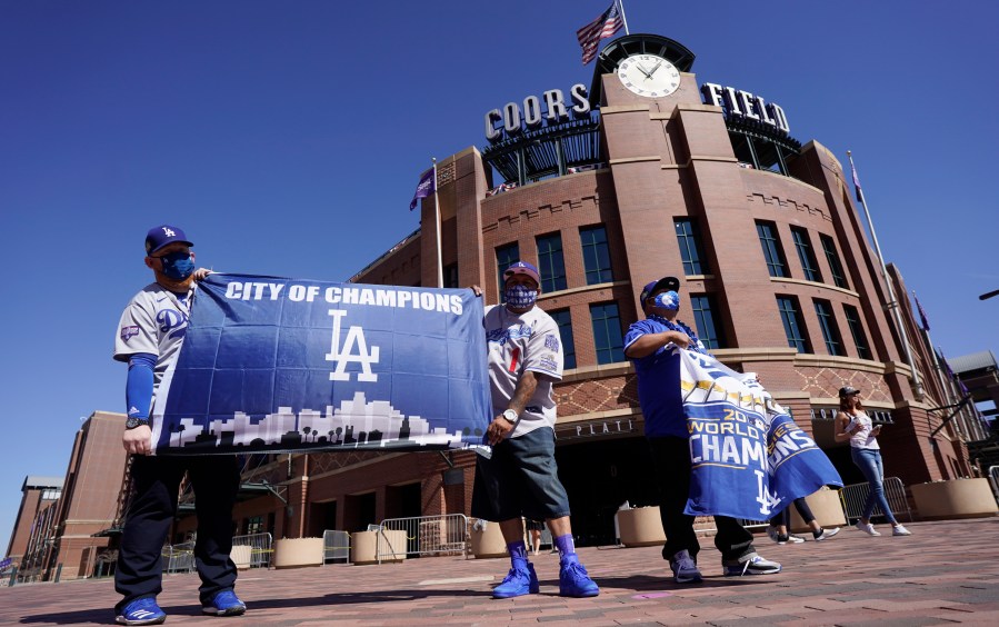 Los Angeles Dodgers fans Oliver Olson, left, of San Diego, Juan Campo and Rudy Soto, both of Los Angeles, hold up flags outside the main entrance to Coors Field in Denver as fans return for the first inning of a baseball game between the Dodgers and Colorado Rockies on April 1, 2021. (David Zalubowski / Associated Press)