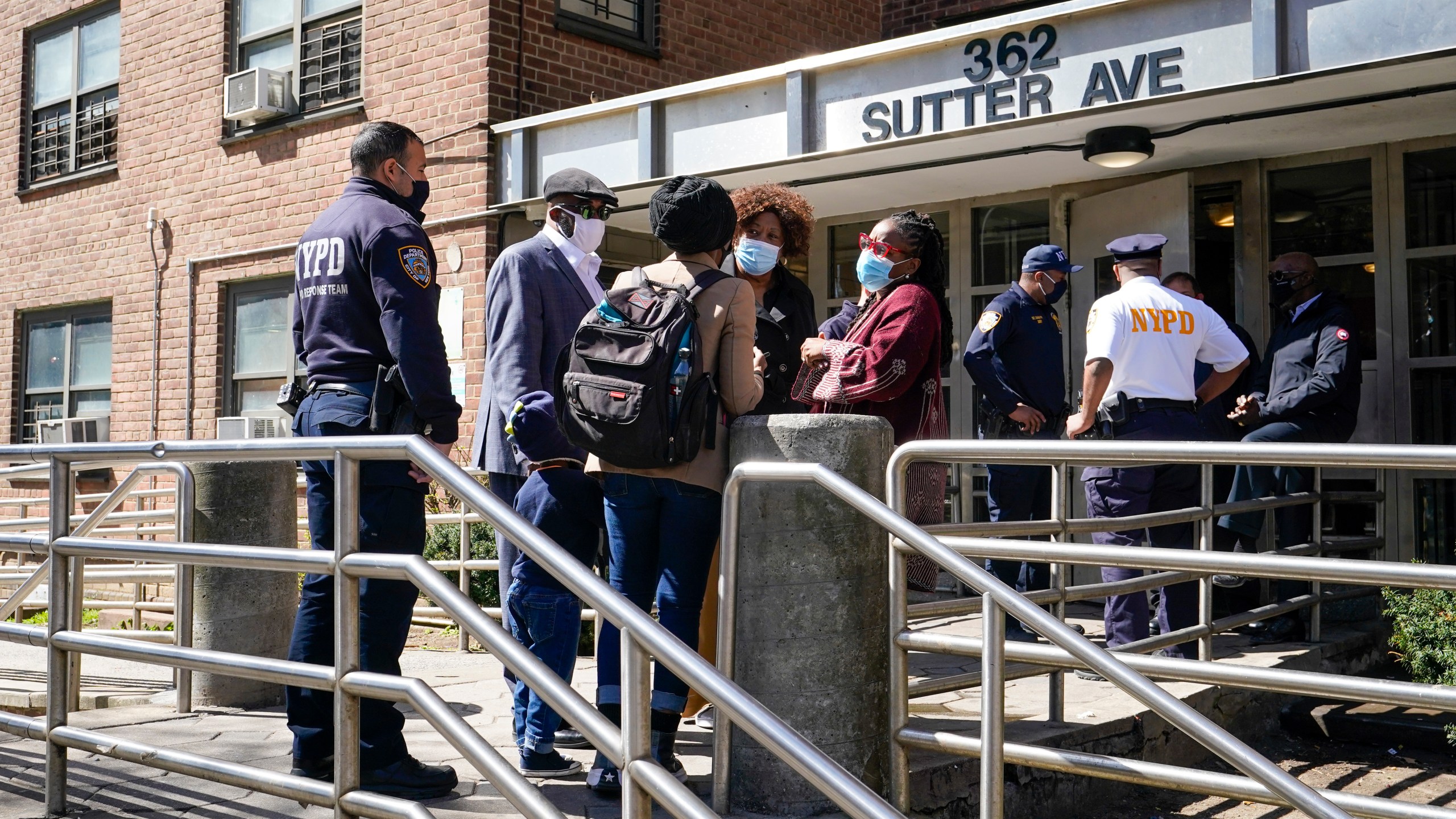 Police officers and community leaders stand outside the building where a man shot the mother of his child and two of her daughters dead before turning the gun on himself, Tuesday, April 6, 2021, in the Brownsville neighborhood of the Brooklyn borough of New York. (AP Photo/Mary Altaffer)