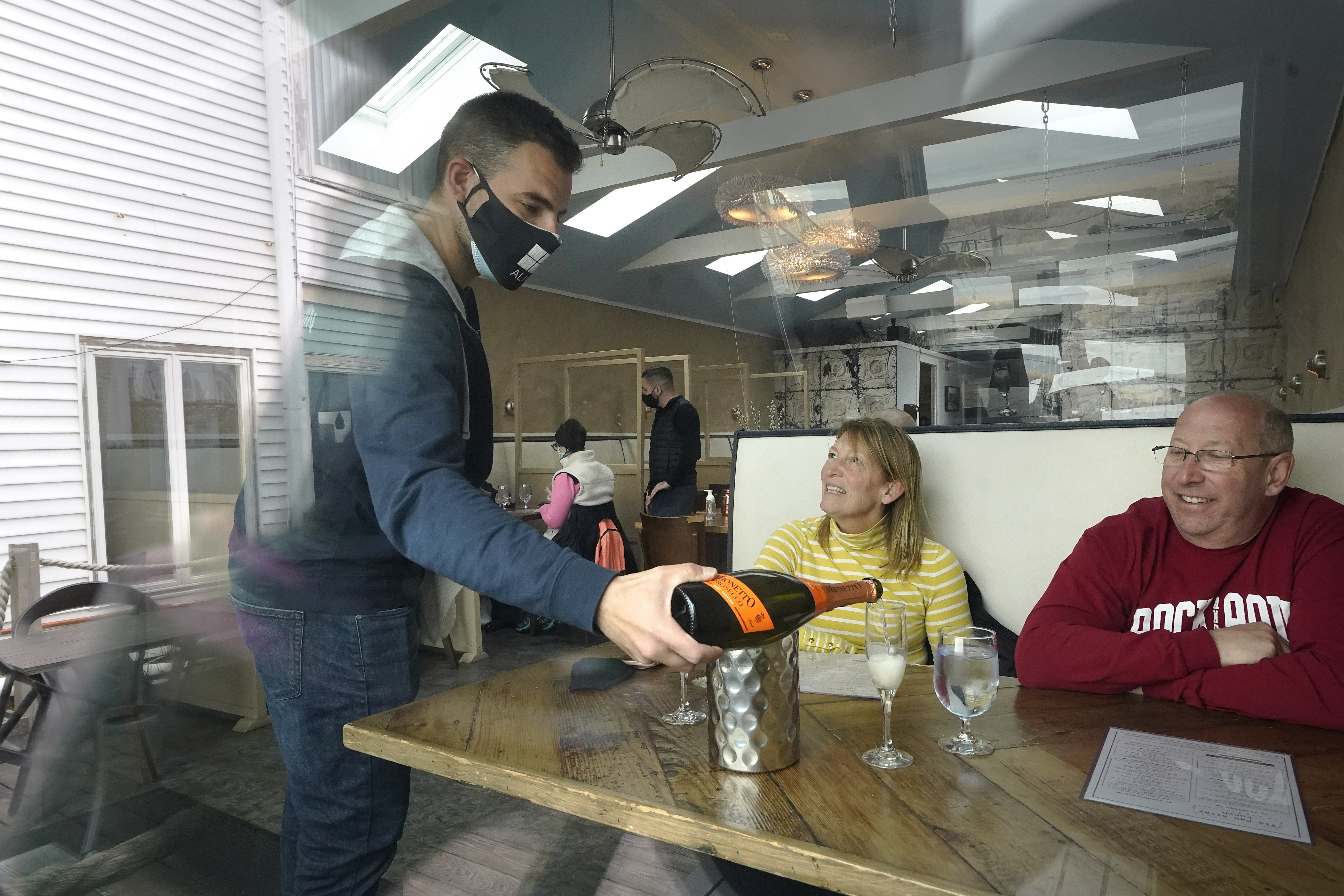 Bartender Denis Angelov, of Provincetown, Mass., left, serves sparking wine to Julie Skaller, left, and her husband David Skaller, right, both of Brewster, N.Y., at Tin Pan Alley restaurant, Tuesday, April 6, 2021, in Provincetown. (AP Photo/Steven Senne)