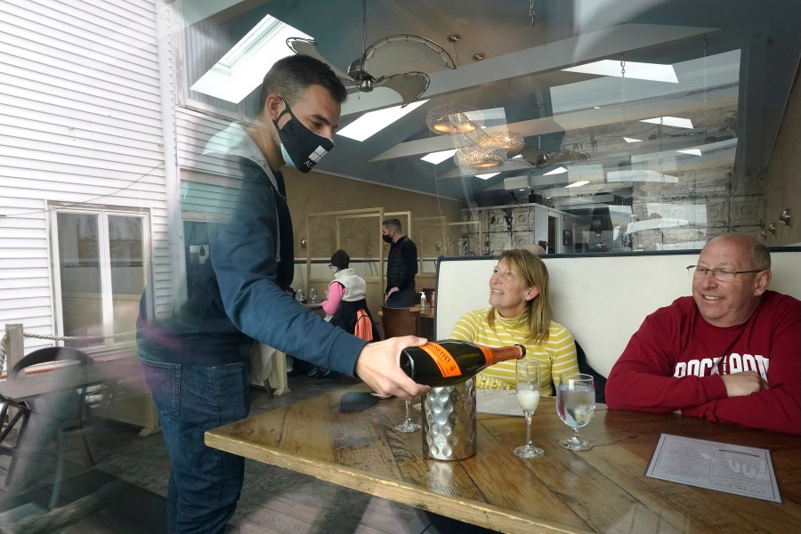 Bartender Denis Angelov, of Provincetown, Mass., left, serves sparking wine to Julie Skaller, left, and her husband David Skaller, right, both of Brewster, N.Y., at Tin Pan Alley restaurant, Tuesday, April 6, 2021, in Provincetown. (AP Photo/Steven Senne)