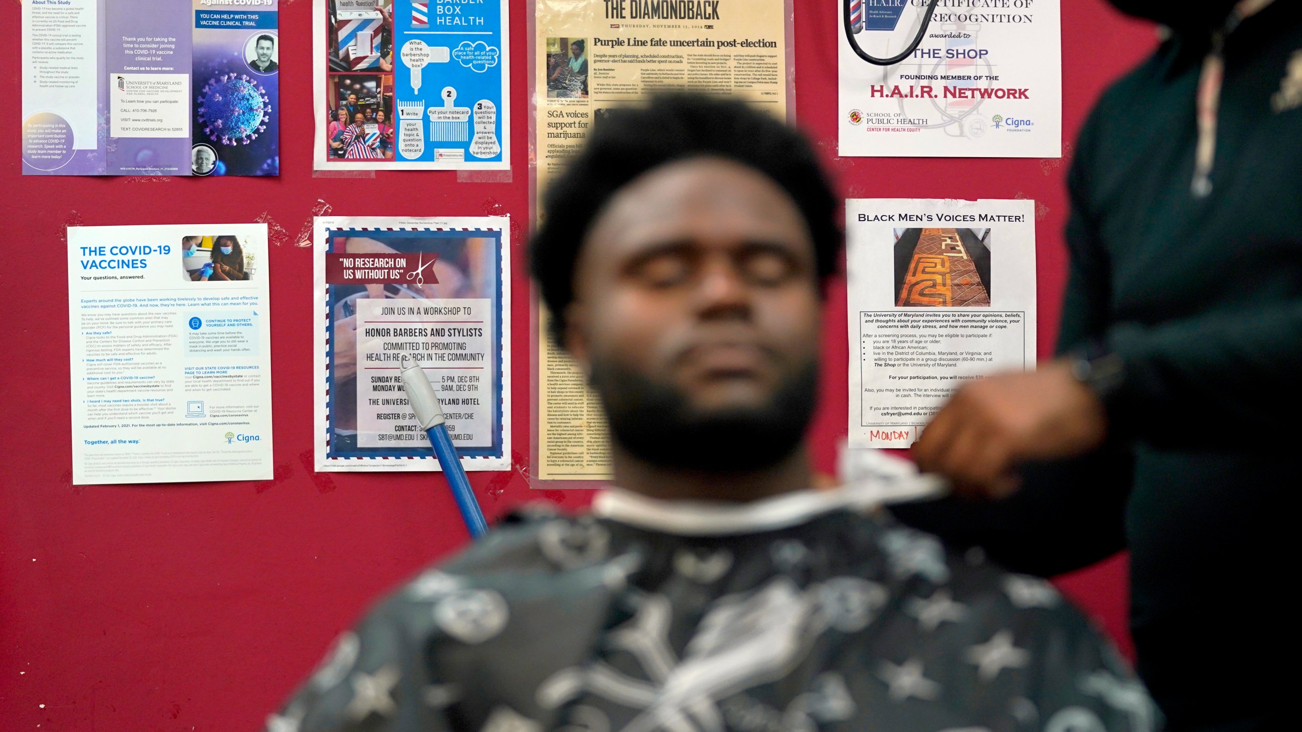 Health literature and a certificate are displayed on the wall as a patron gets a hair cut, Friday, April 9, 2021, in Hyattsville, Md. Barbers at The Shop are members of the Health Advocates In Reach & Research (HAIR) program, which helps barbers and hair stylists to get certified to talk to community members about health. During the COVID-19 pandemic, a team of certified barbers have been providing factual information to customers about vaccines, a topic that historically has not been trusted by members of black communities because of the health abuse the race has endured over the years. (AP Photo/Julio Cortez)