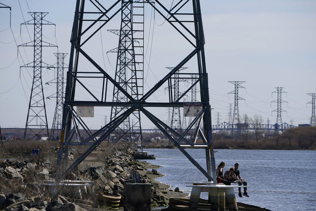 People sit at the base of a transmission tower in North Arlington, N.J., Tuesday, April 6, 2021. (AP Photo/Seth Wenig)