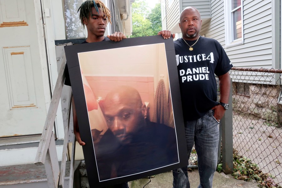 FILE — In this Sept. 3, 2020 file photo, Joe Prude, brother of Daniel Prude, right, and his son Armin, stand with a picture of Daniel Prude in Rochester, N.Y. Newly released transcripts show that a grand jury investigating the police suffocation death of Daniel Prude last year in Rochester, New York, voted 15-5 to clear the three officers involved in his restraint of a criminally negligent homicide charge sought by prosecutors. (AP Photo/Ted Shaffrey, File)