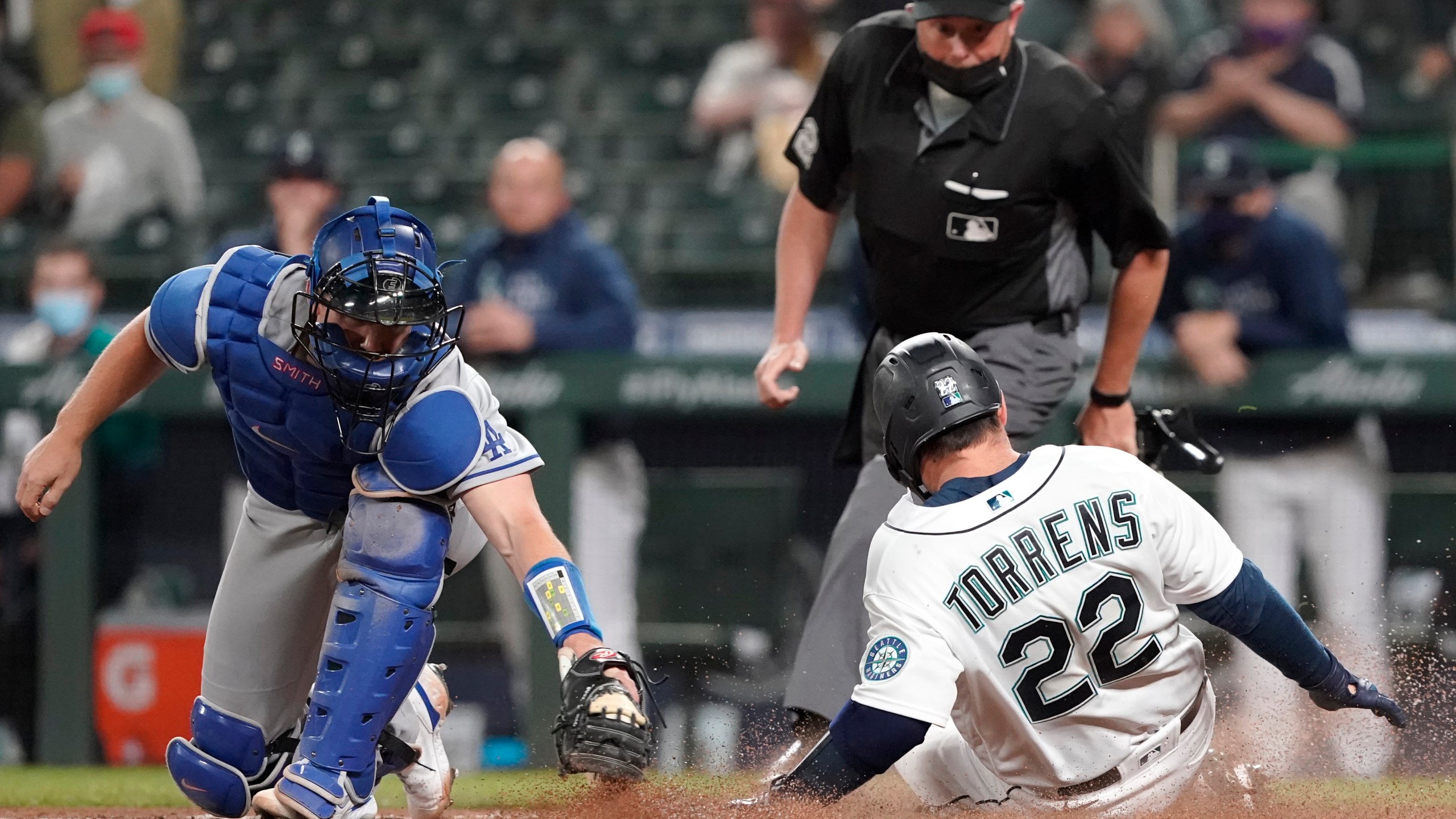 Seattle Mariners' Luis Torrens slides safely home as Los Angeles Dodgers catcher Will Smith attempts the tag during the fourth inning of a baseball game in Seattle on April 19, 2021. (Ted S. Warren / Associated Press)