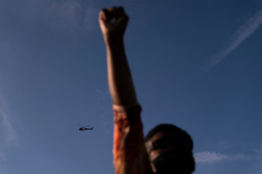 A Los Angeles Police helicopter hovers as Joyce Robertson, foreground, clenches her fist at the intersection of Florence and Normandie Avenues, on April 20, 2021, in Los Angeles, after a guilty verdict was announced at the trial of former Minneapolis police Officer Derek Chauvin for the 2020 death of George Floyd. (AP Photo/Jae C. Hong)