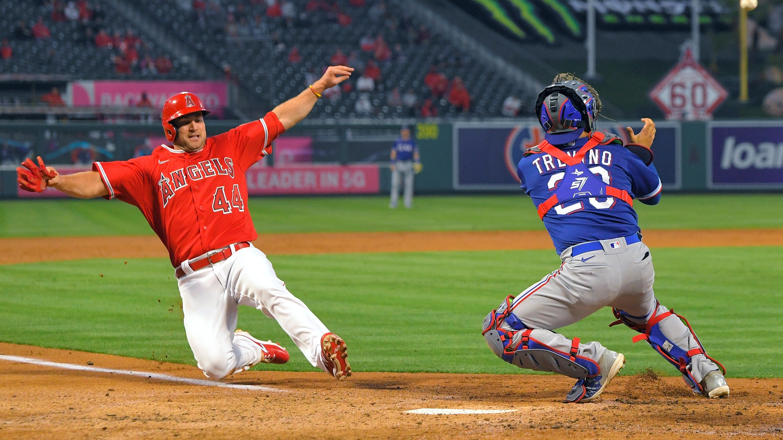 Los Angeles Angels' Scott Schebler, left, scores on a sacrifice fly hit by David Fletcher as Texas Rangers catcher Jose Trevino takes a late throw during the third inning of a baseball game in Anaheim on April 20, 2021. (Mark J. Terrill / Associated Press)