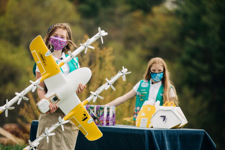 In this April 14, 2021 image provided by Wing LLC., Girl Scouts Alice Goerlich, right, and Gracie Walker pose with a Wing delivery drone in Christiansburg, Va. The company is testing drone delivery of Girl Scout cookies in the area. (Sam Dean/ Wing LLC via AP)