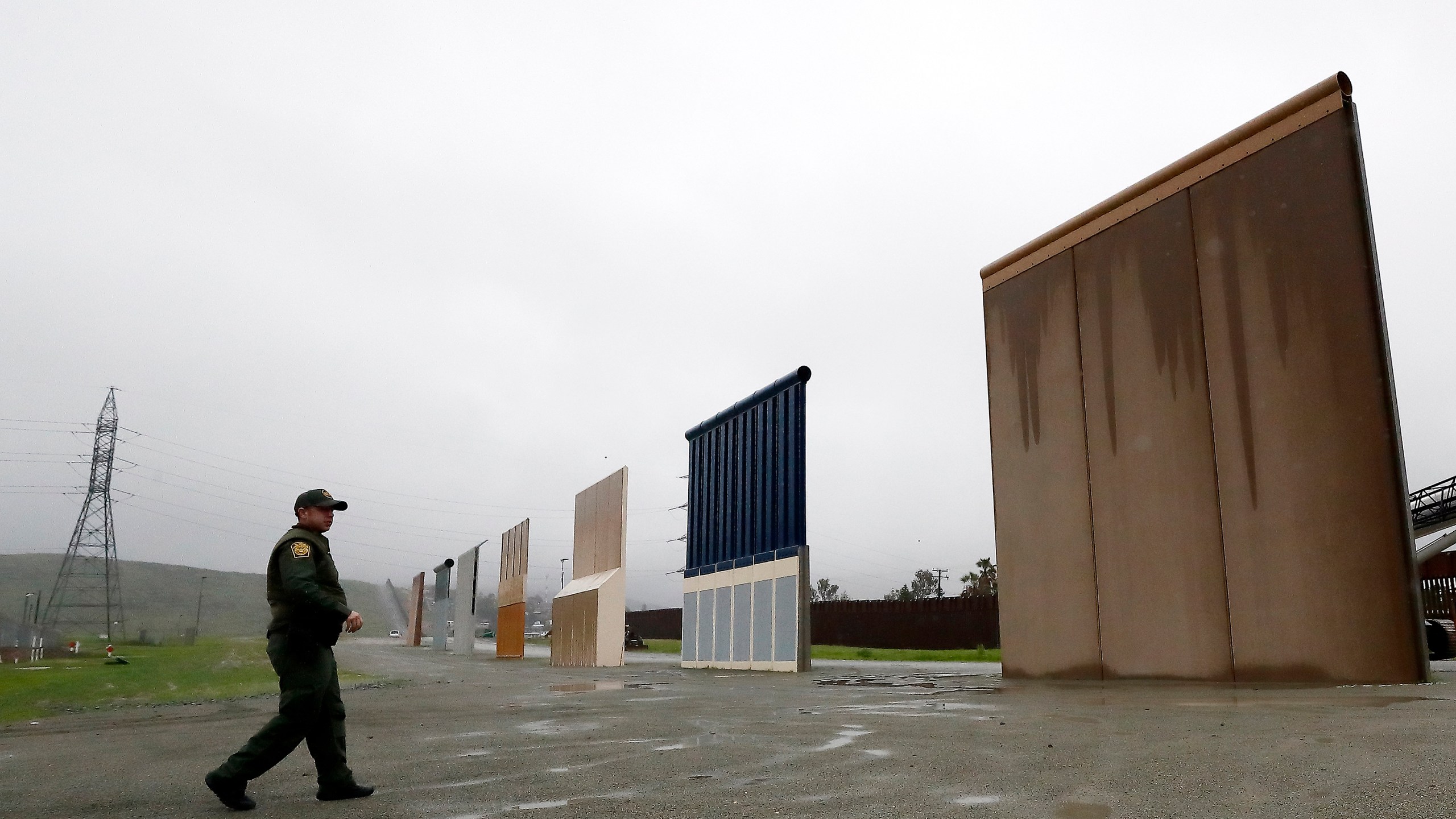 In this Feb. 5, 2019 file photo, U.S. Border Patrol agent Vincent Pirro walks towards prototypes for a border wall in San Diego. The Biden administration says it will begin work to address flooding and soil erosion risks from unfinished walls on the U.S. border with Mexico. It also began providing answers on how it will use unspent money from shutting down one of President Donald Trump's signature domestic projects. The Defense Department says it will use unobligated money for military construction projects for its initial purpose. (AP Photo/Gregory Bull, File)