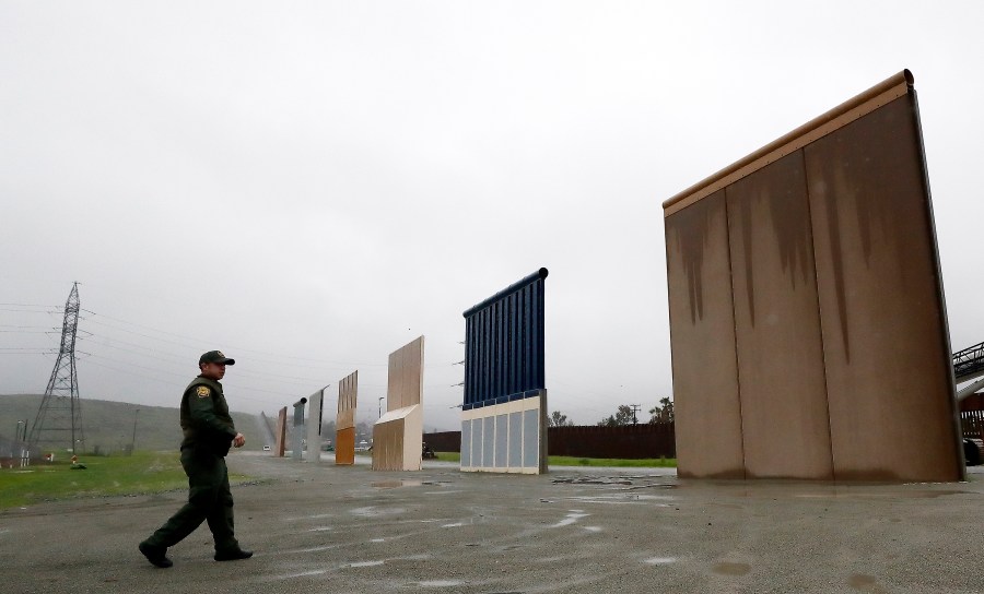 In this Feb. 5, 2019 file photo, U.S. Border Patrol agent Vincent Pirro walks towards prototypes for a border wall in San Diego. The Biden administration says it will begin work to address flooding and soil erosion risks from unfinished walls on the U.S. border with Mexico. It also began providing answers on how it will use unspent money from shutting down one of President Donald Trump's signature domestic projects. The Defense Department says it will use unobligated money for military construction projects for its initial purpose. (AP Photo/Gregory Bull, File)