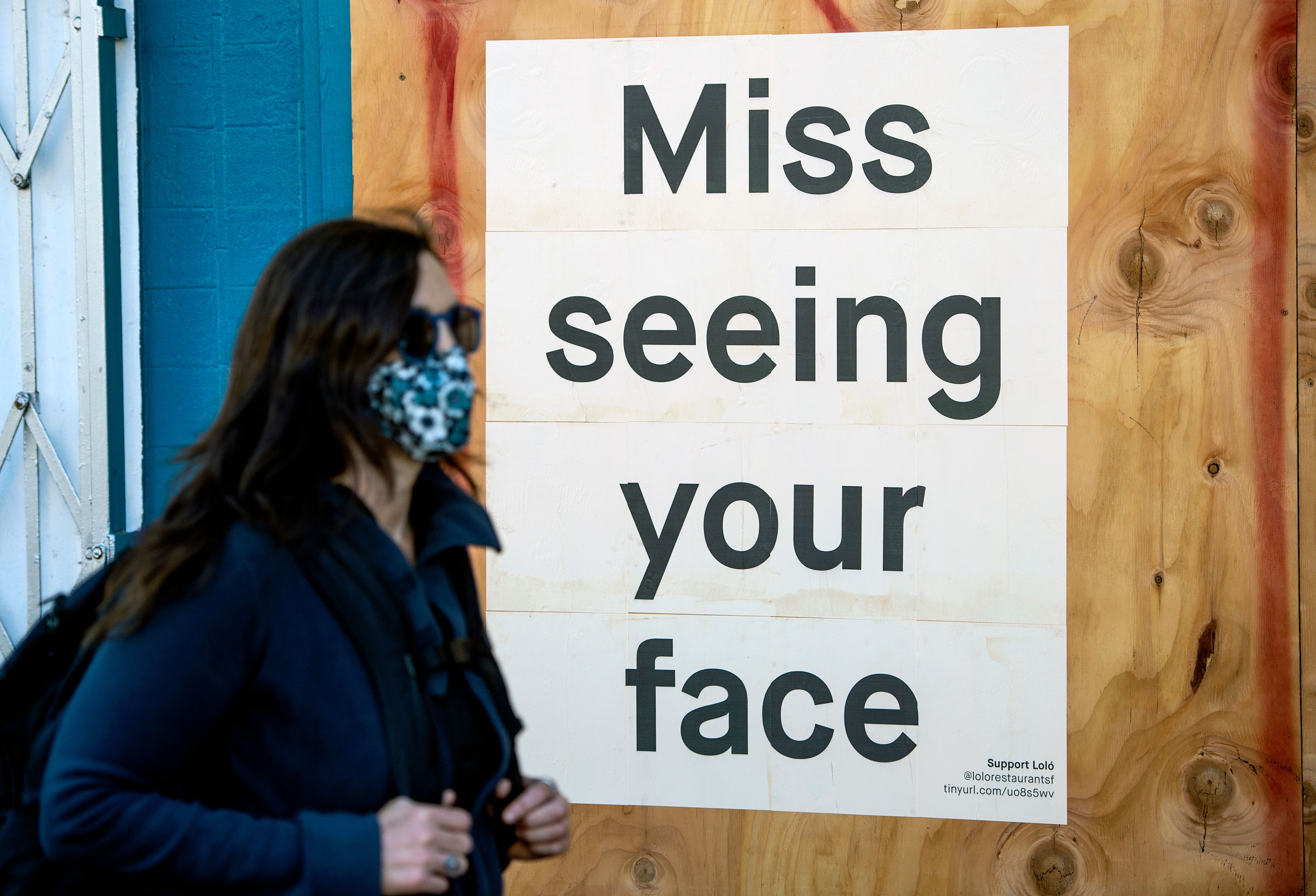 A woman in a face mask walks by a sign posted on a boarded up restaurant in San Francisco on April, 1, 2020, during the novel coronavirus outbreak. (Josh Edelson / AFP via Getty Images)