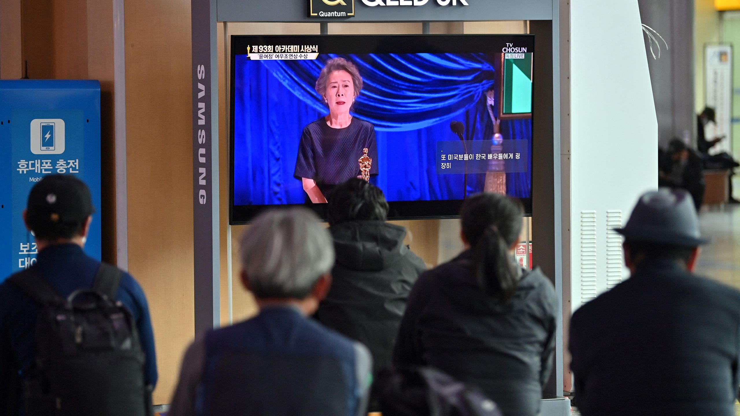 People watch a television screen broadcasting live footage of South Korea's first Oscar-winning actress Youn Yuh-jung speaking at the 93rd Academy Awards ceremony held in Los Angeles, at Seoul railway station in Seoul on April 26, 2021. (JUNG YEON-JE/AFP via Getty Images)