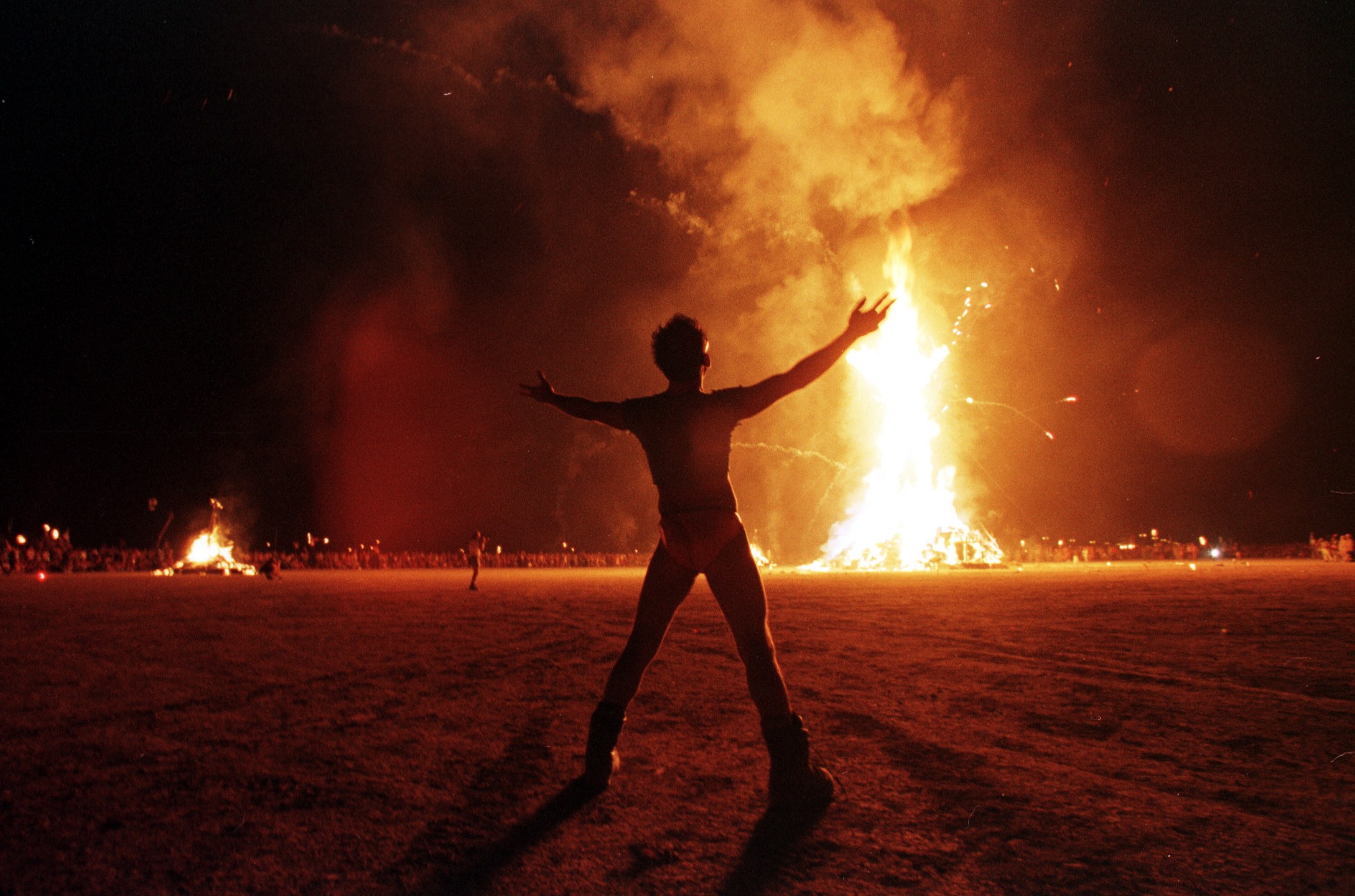 A Burning Man participant holds up his arms as the wooden man effigy is burned at the conclusion of the week-long festival on Sept. 6, 1998. (MIKE NELSON/AFP via Getty Images)