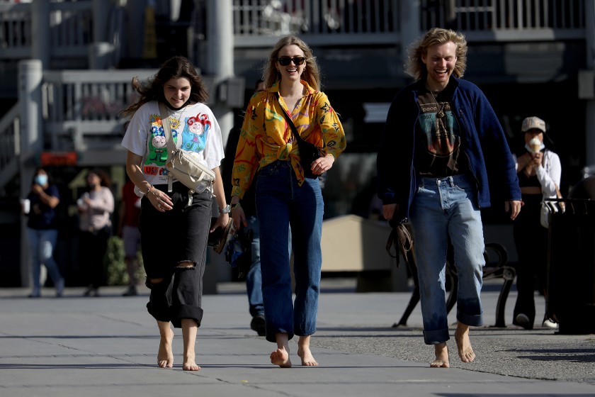 Three women walk without masks along the boardwalk in Redondo Beach on Tuesday. Under new CDC guidelines, fully vaccinated Americans don’t need to wear masks outdoors anymore unless they are in a big crowd of strangers. (Gary Coronado / Los Angeles Times)