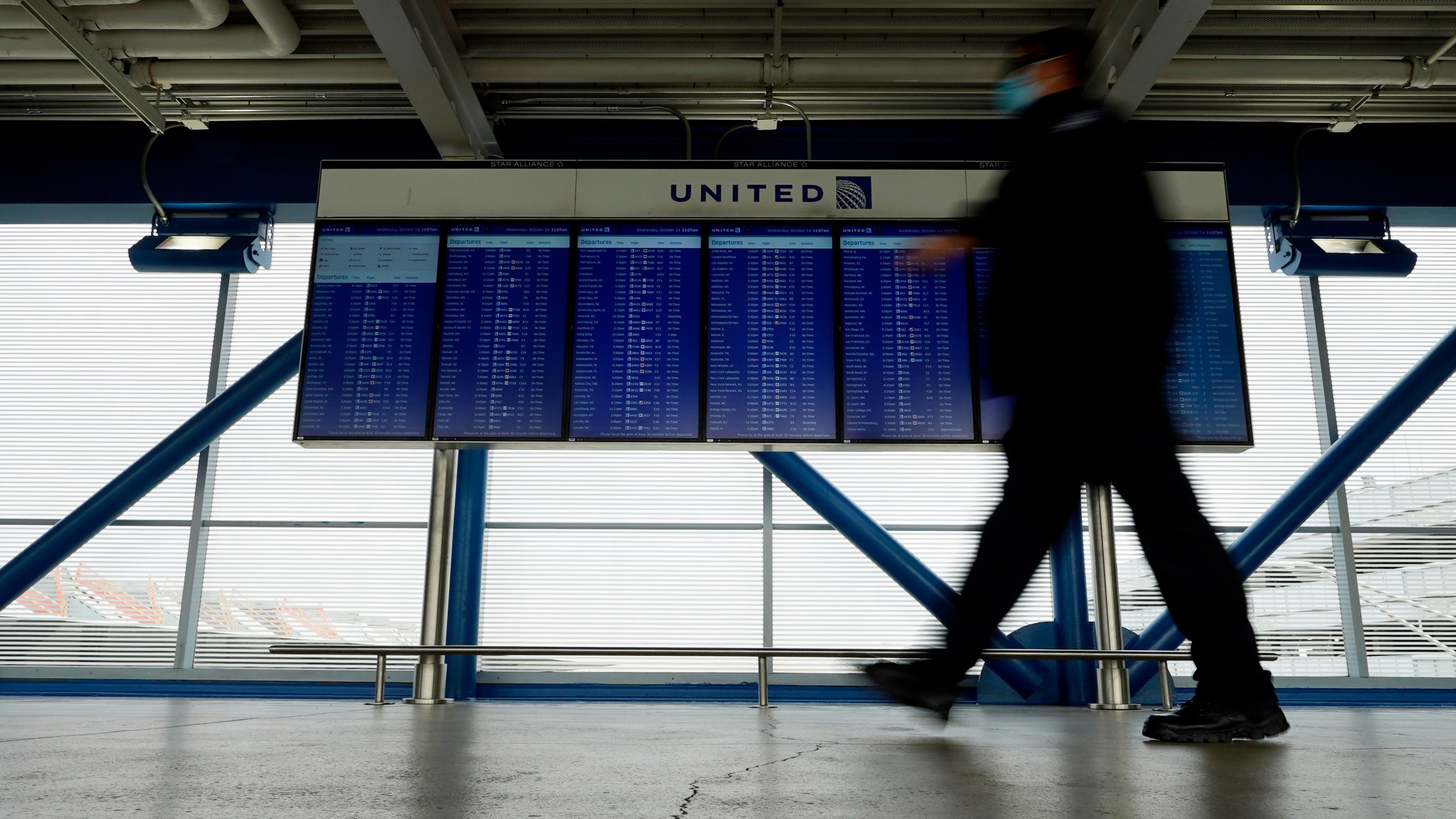 In this Oct. 14, 2020 file photo, a TSA staff wears mask as he walks past flight information screens show flight status information at O'Hare International Airport in Chicago. (AP Photo/Nam Y. Huh)