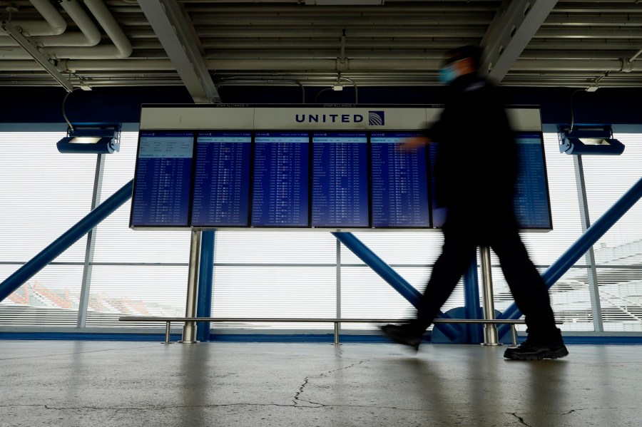 In this Oct. 14, 2020 file photo, a TSA staff wears mask as he walks past flight information screens show flight status information at O'Hare International Airport in Chicago. (AP Photo/Nam Y. Huh)