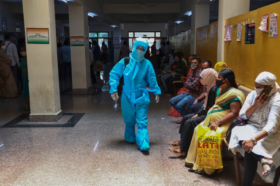 An Indian woman in personal protective suit walks towards a COVID-19 ward of a hospital as others waits for their test results in Hyderabad, India, Thursday, April 29, 2021. (AP Photo/Mahesh Kumar A.)