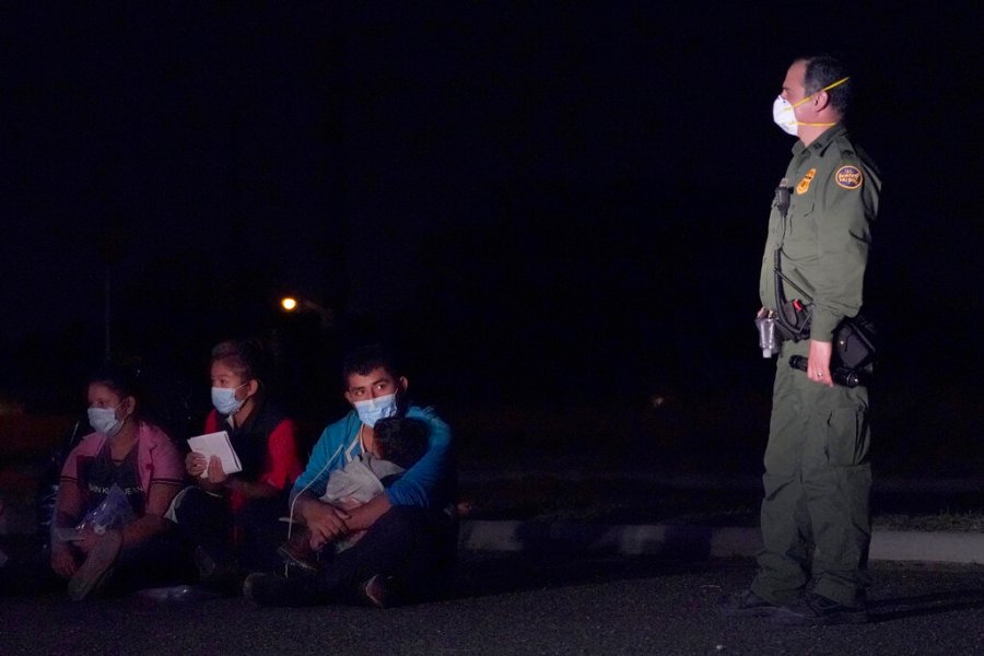 In this March 24, 2021 photo, a migrant man, center, holds a child as he looks at a U.S. Customs and Border Protection agent at an intake area after crossing the U.S.-Mexico border, early Wednesday, March 24, 2021, in Roma, Texas. (AP Photo/Julio Cortez)