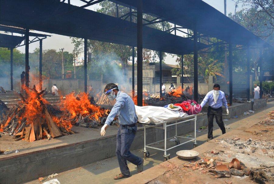 In this May 1, 2021, file photo, relatives carry the body of a person who died of COVID-19 as multiple pyres of other COVID-19 victims burn at a crematorium in New Delhi, India. (AP Photo/Amit Sharma, File)