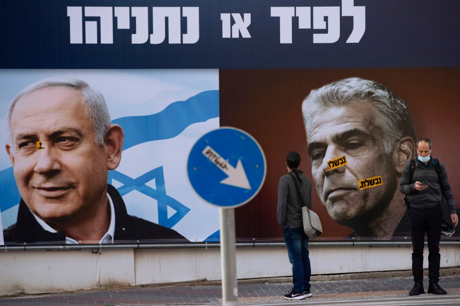 In this Sunday, March. 14, 2021 file photo, people stand in front of an election campaign billboard for the Likud party showing a portrait of its leader Prime Minister Benjamin Netanyahu, left, and opposition party leader Yair Lapid, in Ramat Gan, Israel. Israel's President Reuven Rivlin has tapped opposition leader Yair Lapid to form a new government, a step that could lead to the end of the lengthy rule of Prime Minister Benjamin Netanyahu. Rivlin announced his decision on live television a day after Netanyahu failed to cobble together a governing coalition by a midnight deadline. (AP Photo/Oded Balilty, File)