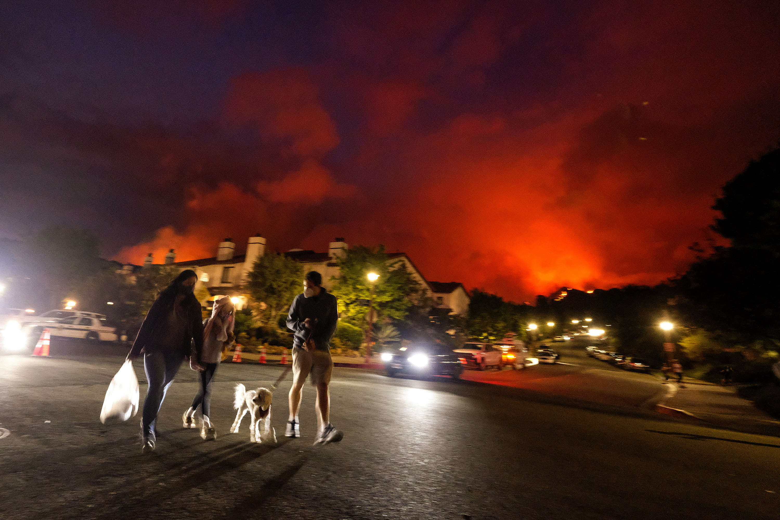 Residents walk a dog as a brush fire burns behind homes in the Pacific Palisades area of Los Angeles on Saturday, May 15, 2021. (AP Photo/Ringo H.W. Chiu)