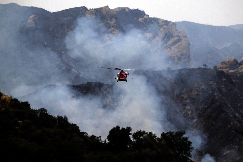 A firefighting helicopter prepares to drop water onto a wildfire in the Pacific Palisades area of Los Angeles, Sunday, May 16, 2021. (AP Photo/Ringo H.W. Chiu)