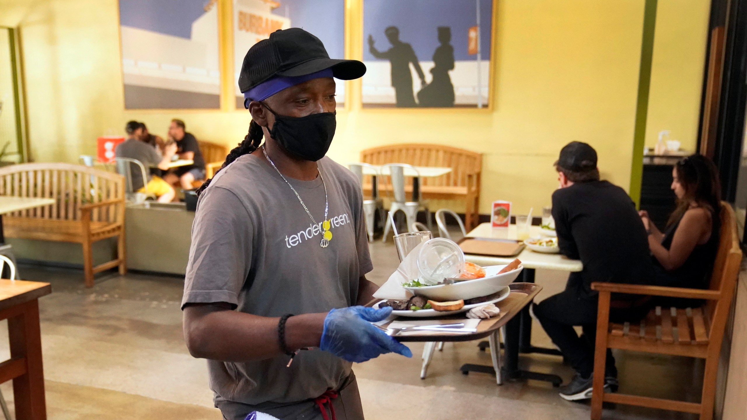 A worker in a face mask clears tables inside a covered patio in Burbank amid the COVID-19 pandemic on May 18, 2021. (Marcio Jose Sanchez / Associated Press)