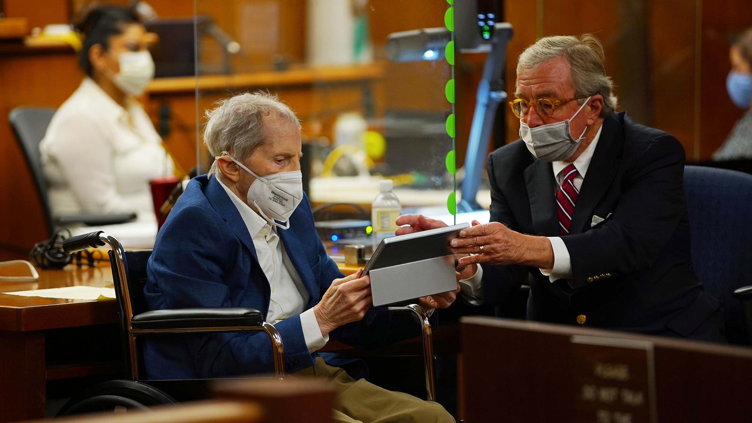 Defense attorney Dick DeGuerin, right, gives Robert Durst a device to read the real time spoken script as he appears in a courtroom as Judge Mark E. Windham gives last instructions to jurors before attorneys begin opening statements at the Los Angeles County Superior Court on May 18, 2021. (Al Seib/Los Angeles Times)