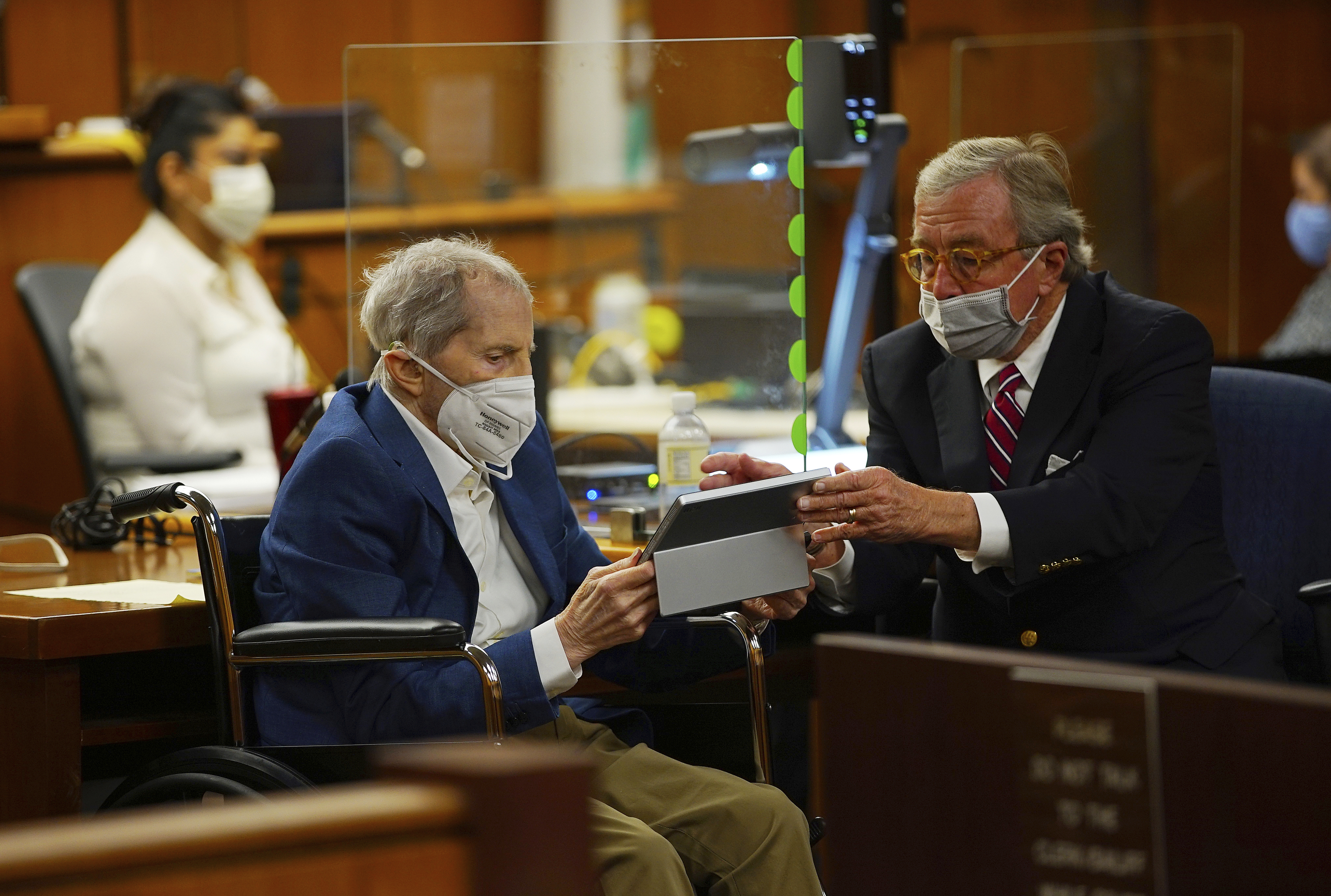 Defense attorney Dick DeGuerin, right, gives Robert Durst a device to read the real time spoken script as he appears in a courtroom as Judge Mark E. Windham gives last instructions to jurors before attorneys begin opening statements at the Los Angeles County Superior Court on May 18, 2021. (Al Seib/Los Angeles Times)